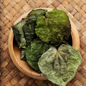 A bowl filled with kawakawa dried leaves sits atop a woven table, showcasing natural textures and earthy tones.