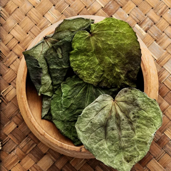 A bowl filled with kawakawa dried leaves sits atop a woven table, showcasing natural textures and earthy tones.