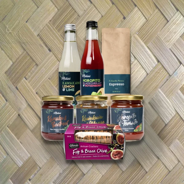 Atutahi gourmet New Zealand gift set with Kawakawa Lemon & Lime and Horopito Blackcurrant drinks, artisan chutneys, Kiwikai Espresso, and Olina's Fig & Black Olive crackers on a woven mat background.