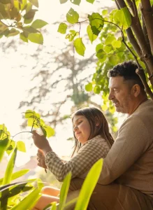 A man and a young girl enjoy a sunny day together, sitting side by side and smiling in the warm sunlight.