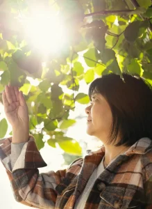 A woman reaches high with her hand, trying to touch the sun shining brightly above her.